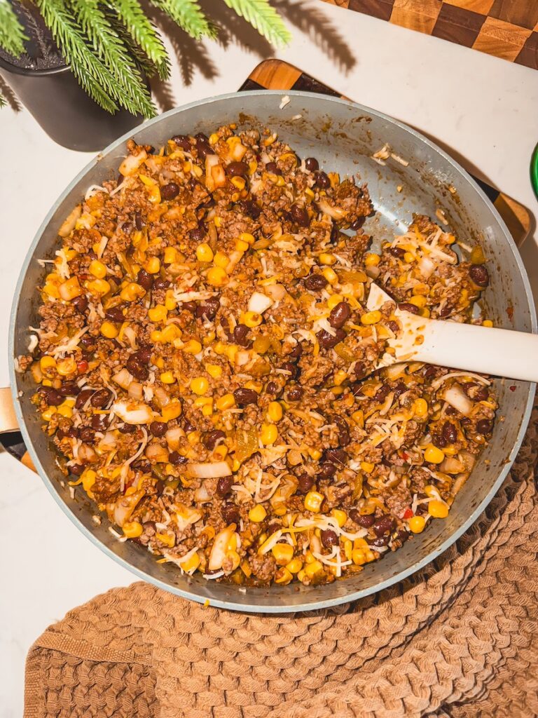 A skillet with ground beef mixture with shredded cheese.