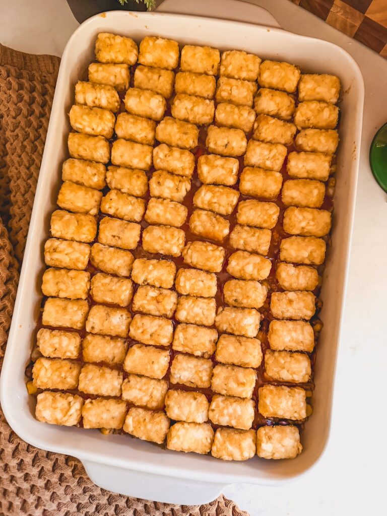Mexican tater tot casserole in a white baking dish with tater tots lined up on top.