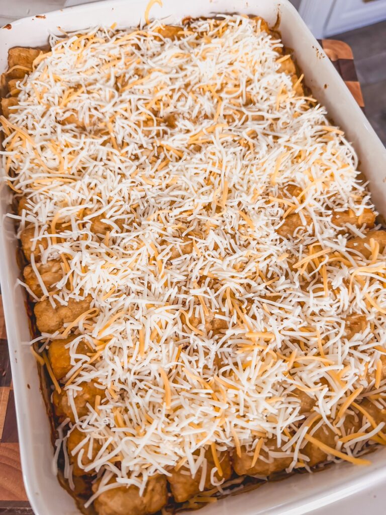 A white baking dish with Mexican tater tot casserole with shredded cheese on top.