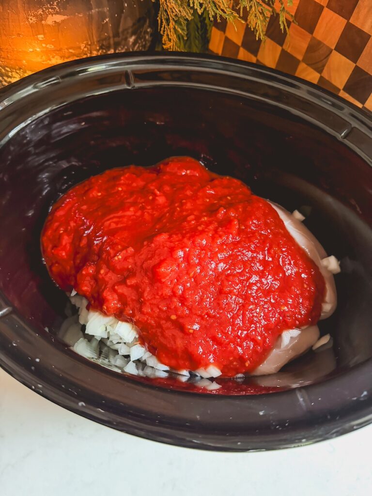 A slow cooker with chicken, tomatoes, onion.