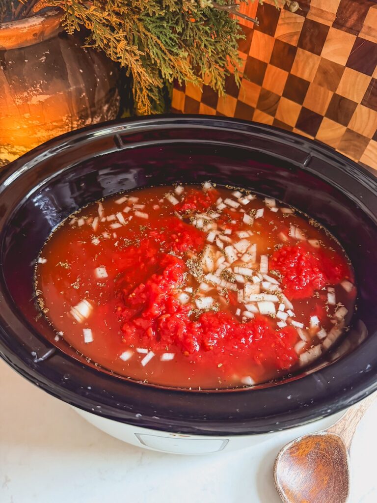 A slow cooker with chicken, broth, tomato, onion, for slow cooker chicken tortellini soup.