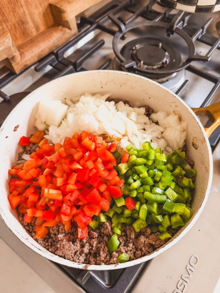 A saute pan cooking beef, peppers, and onions on the stovetop.