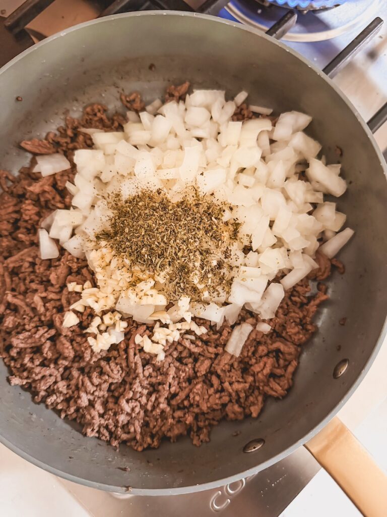 A skillet with ground beef, onion, spices, and garlic.