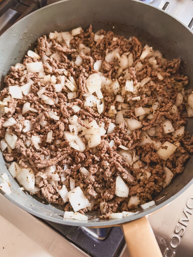 A skillet with ground beef and onion on the stovetop.