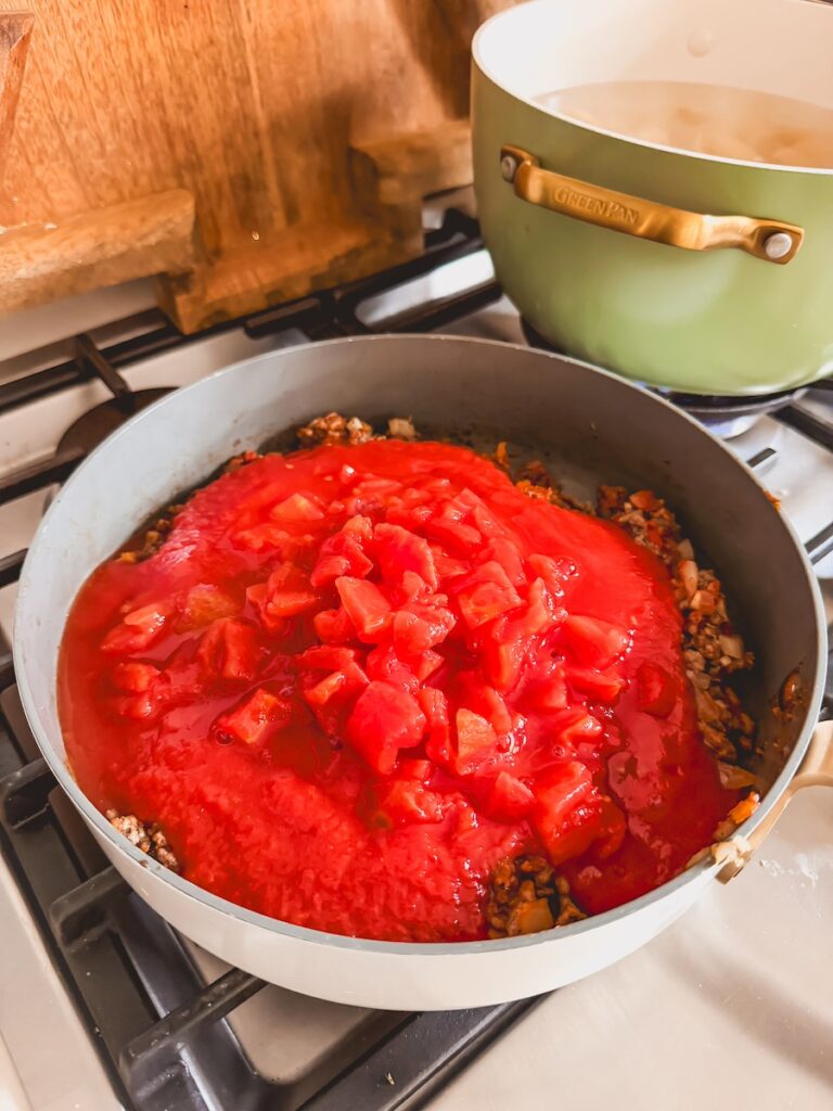 A skillet with beef, tomatoes, spices, and onion cooking.