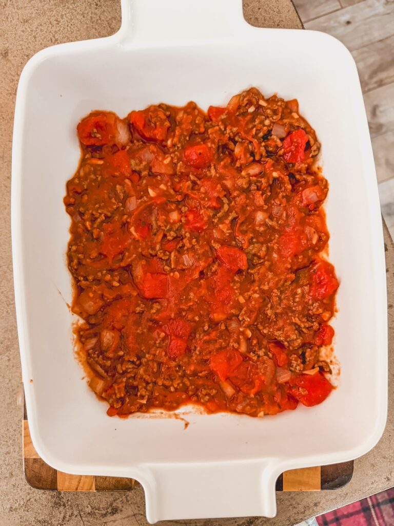 A white casserole dish with beef and tomato sauce in the bottom.