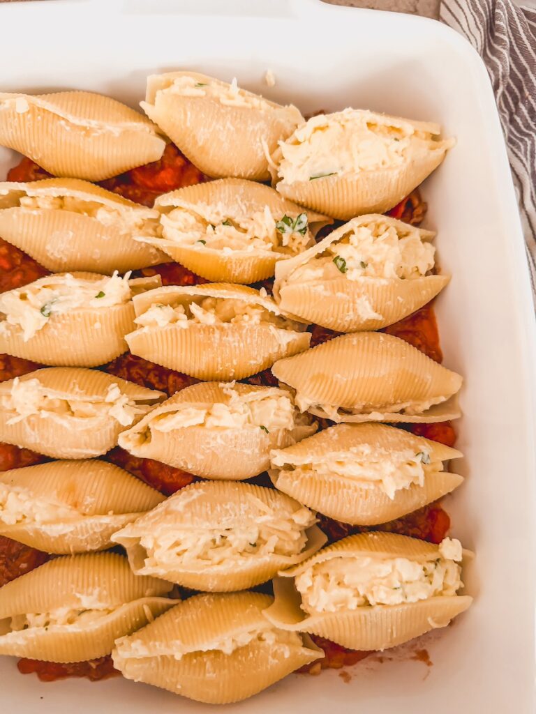 A white baking dish with shells stuffed with ricotta.