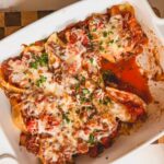 A white baking dish with beef and ricotta stuffed shells with some scooped out.