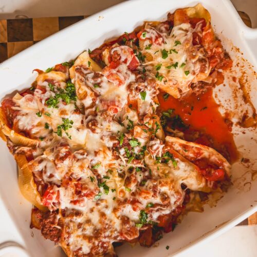 A white baking dish with beef and ricotta stuffed shells with some scooped out.