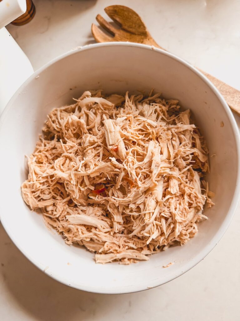 Shredded chicken in a white bowl with a wooden spoon in the background.