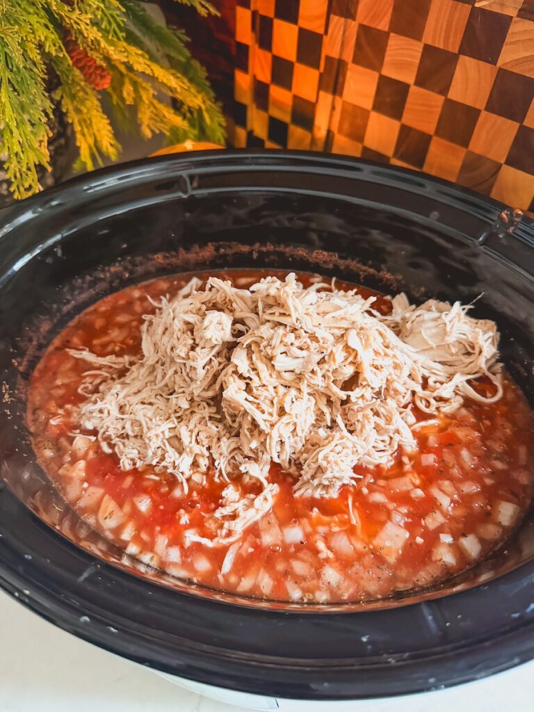 A slow cooker with shredded chicken, tomatoes, chicken broth and onion base.