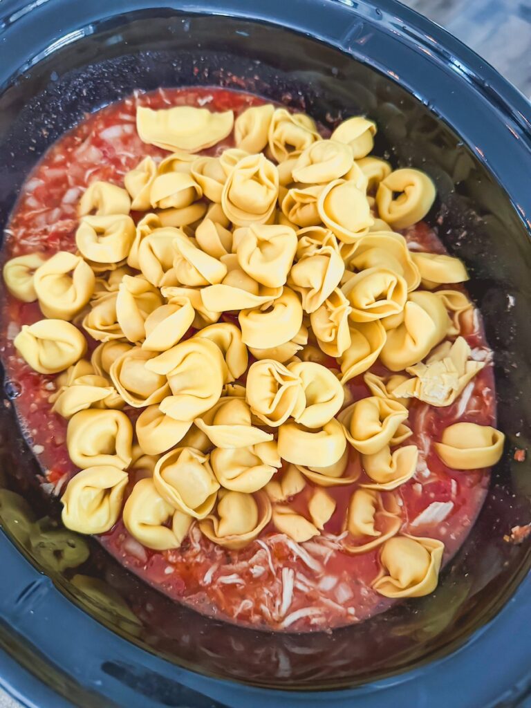 Cheese tortellini is added to the slow cooker for slow cooker chicken tortellini soup.