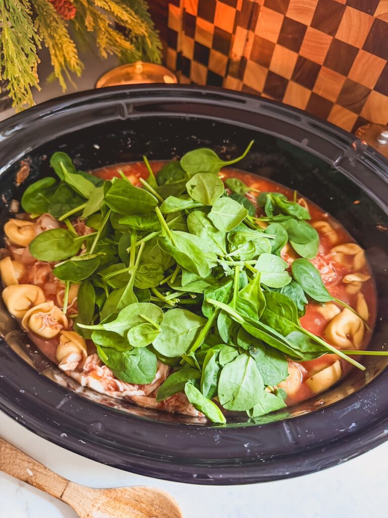 Baby spinach is added to slow cooker chicken tortellini soup.