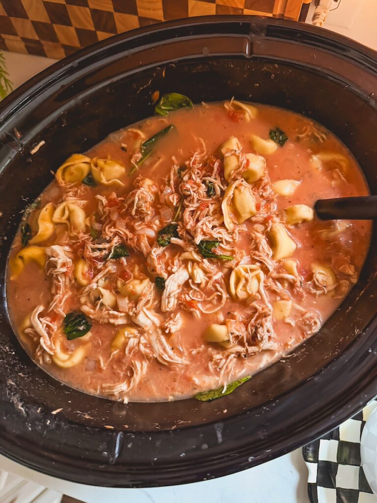 Slow cooker chicken tortellini soup with a ladle in it.