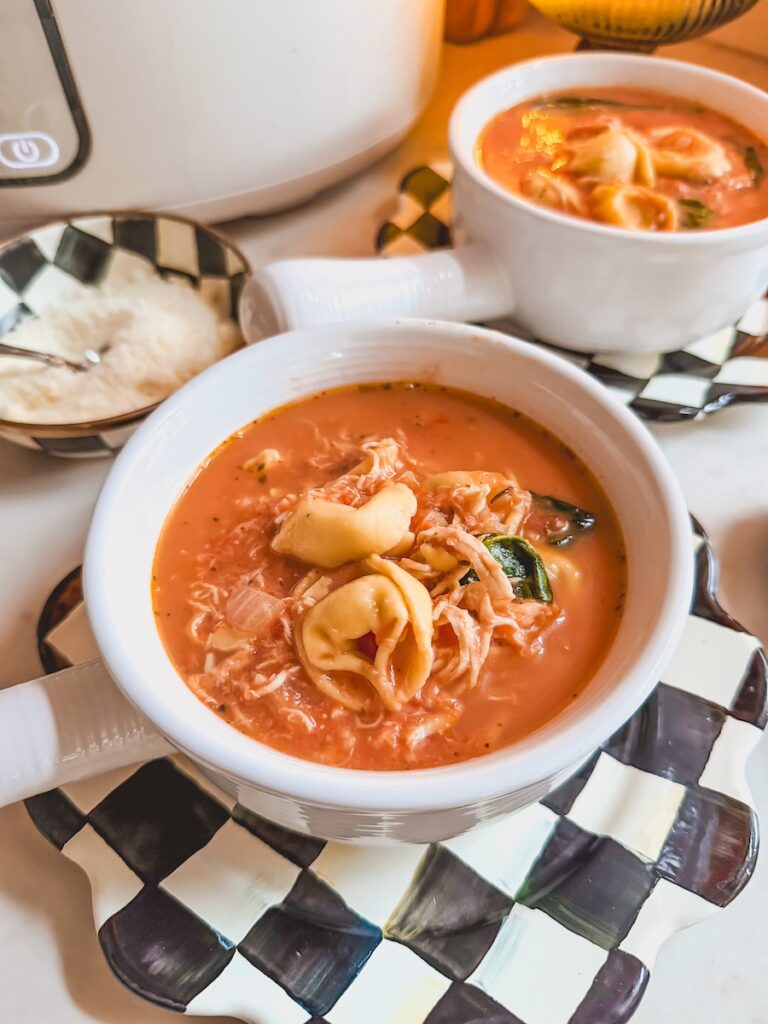 A close up image of slow cooker chicken tortellini soup on black and white checkered plates.