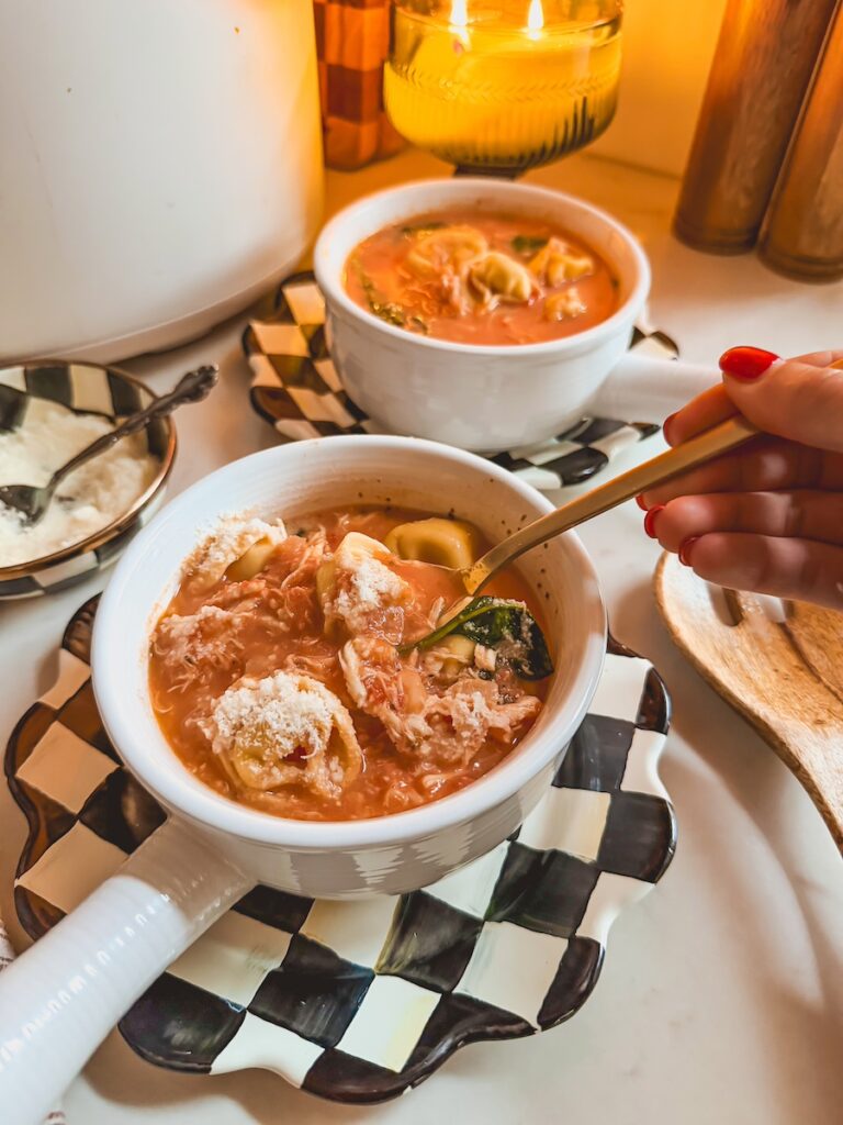 A hand with a gold spoon with slow cooker chicken tortellini soup in white bowls.