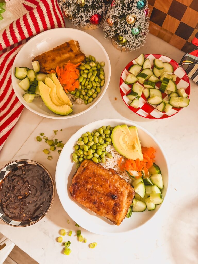 assembling the teriyaki bowls with salmon, white rice, carrots, cucumber and edamame 