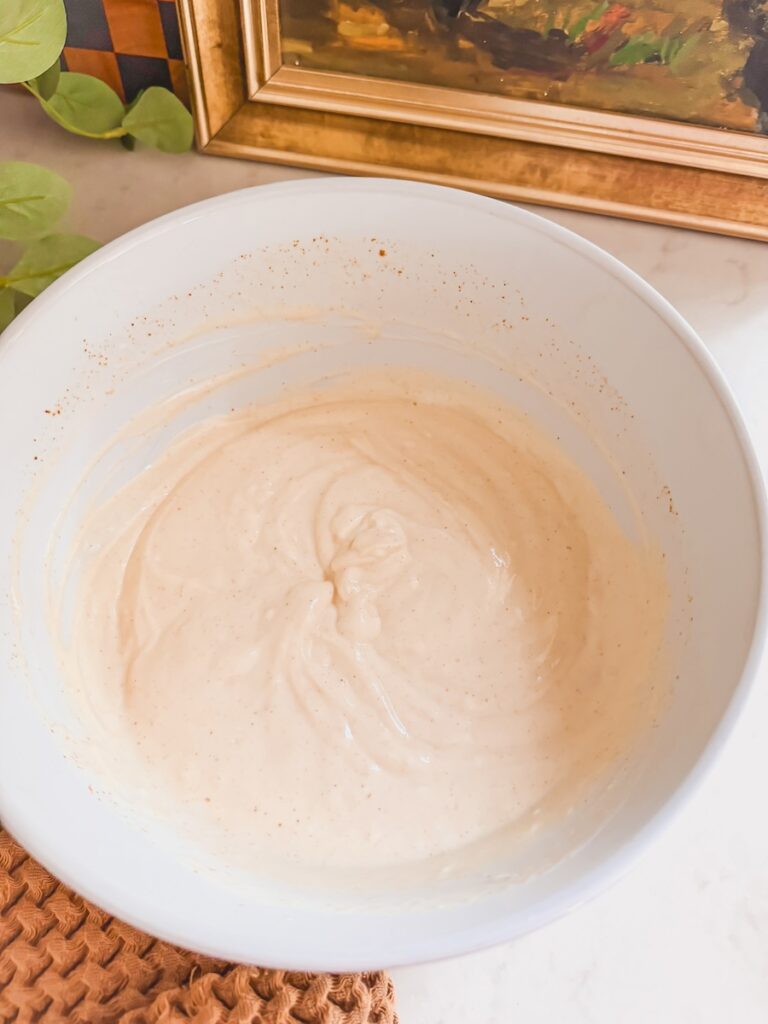 cheesy potatoes creamy sauce in white bowl on counter with picture frame in background