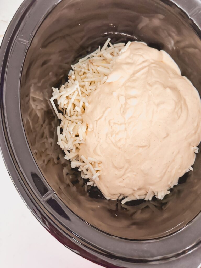 uncooked frozen hashbrowns with creamy sauce on top, in bottom of slow cooker