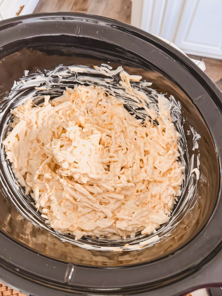 uncooked frozen hashbrowns mixed together with creamy sauce in bottom of slow cooker