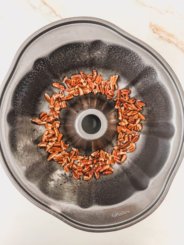 A bundt pan with chopped pecans in the bottom.
