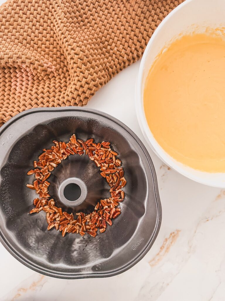 A bundt pan with chopped nuts next to a bowl of mixed cake batter for Baileys Irish Cream Cake.