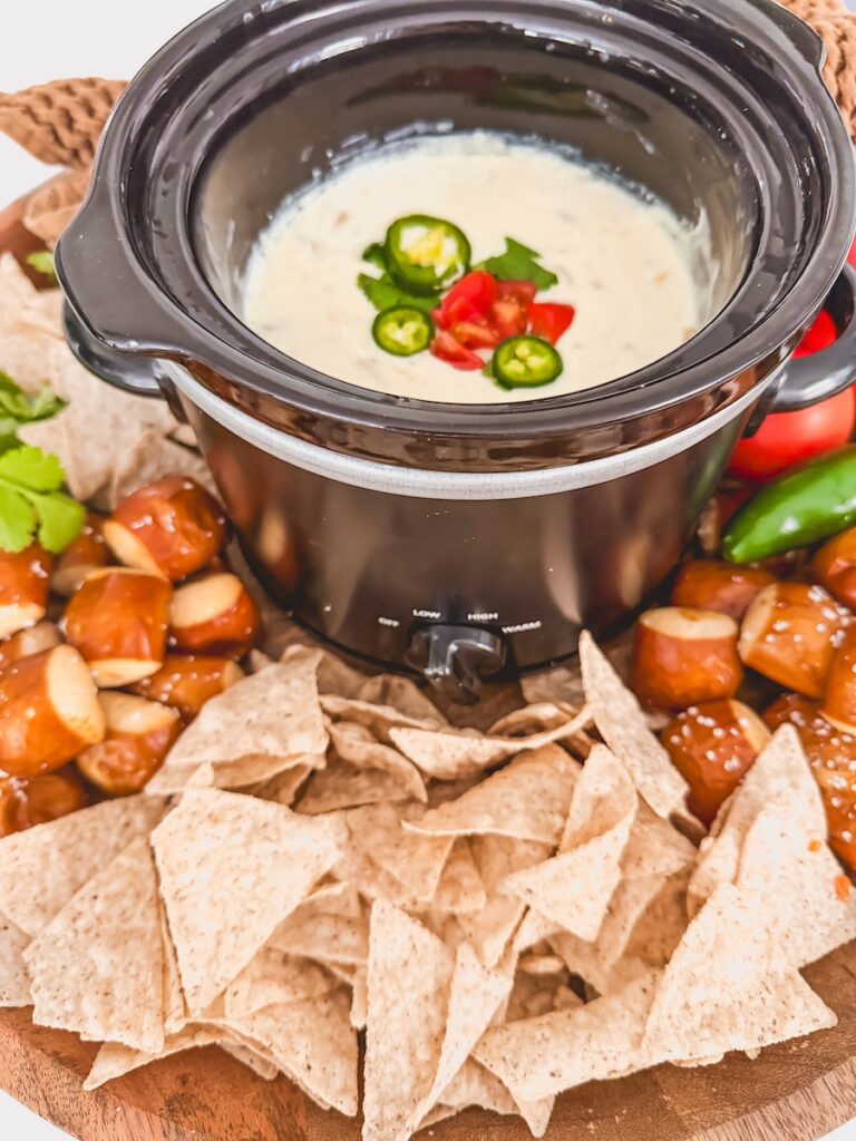 Side view of crock pot queso in slow cooker with chips, pretzels and vegetables around it