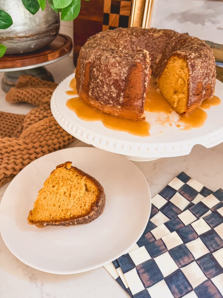 Baileys Irish Cream Bundt Cake on a white cake stand with a slice out on a white plate in front.