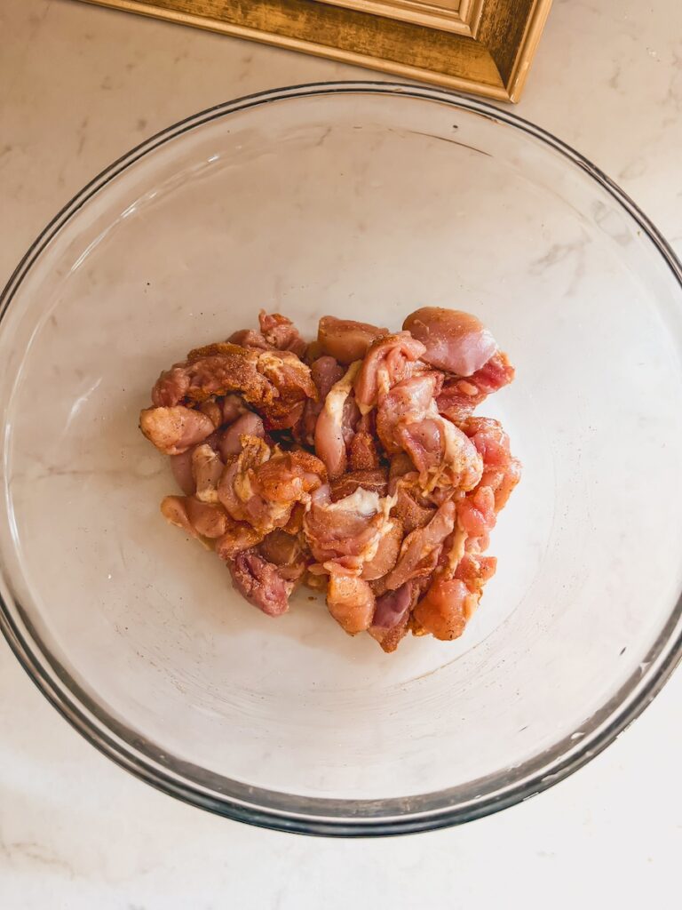 Cut up chicken in a glass bowl with spices.