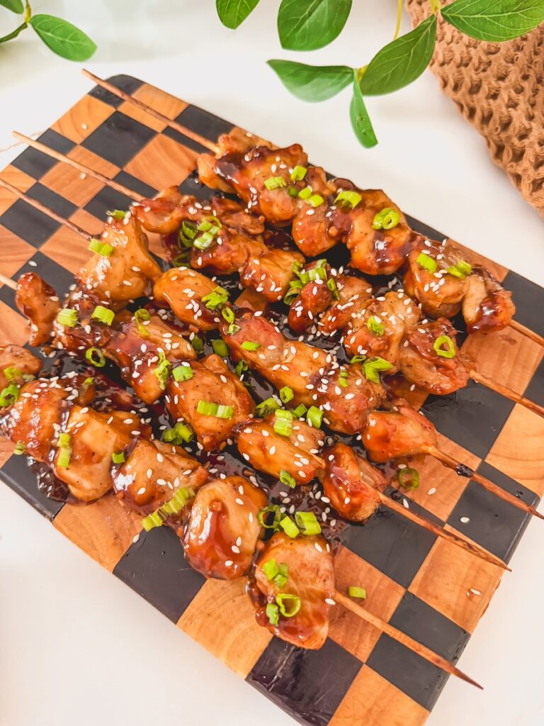 Air fryer chicken teriyaki skewers garnished with scallions on a checkered cutting board.