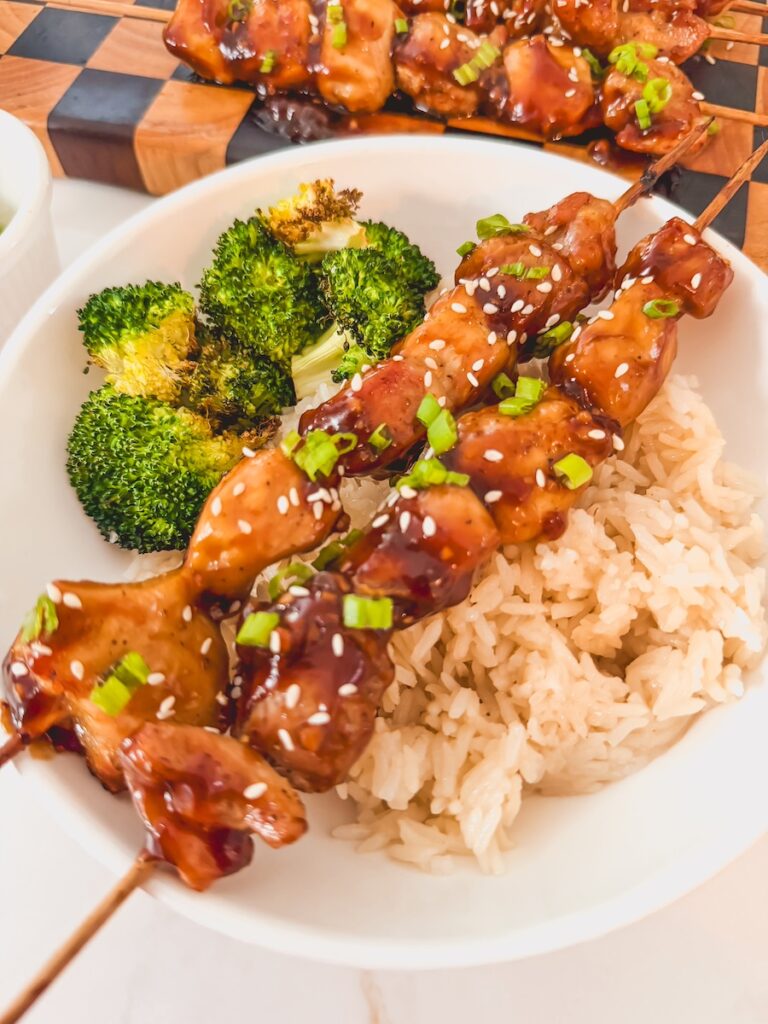 Air fryer chicken teriyaki skewers over white rice with broccoli in a white bowl.