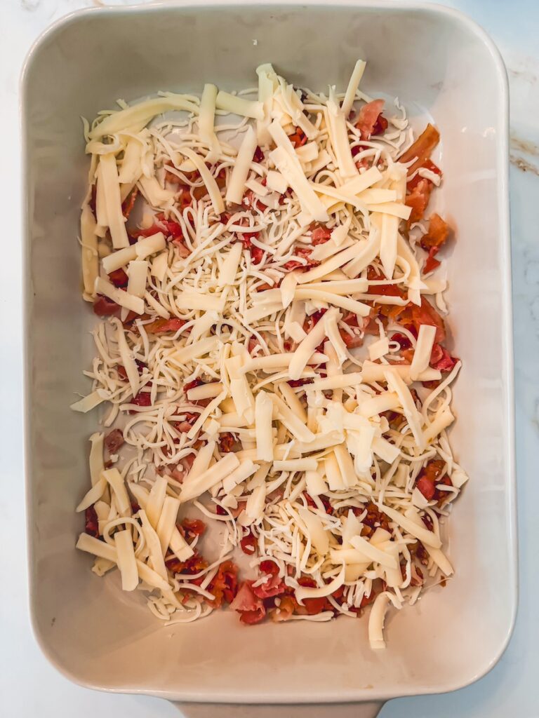 A white baking dish with vegetables and shredded cheese in the bottom.