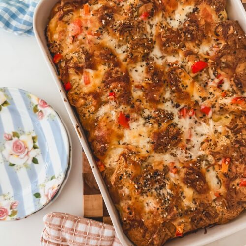 Baked croissant breakfats casserole in a baking dish with blue striped plates on the side.