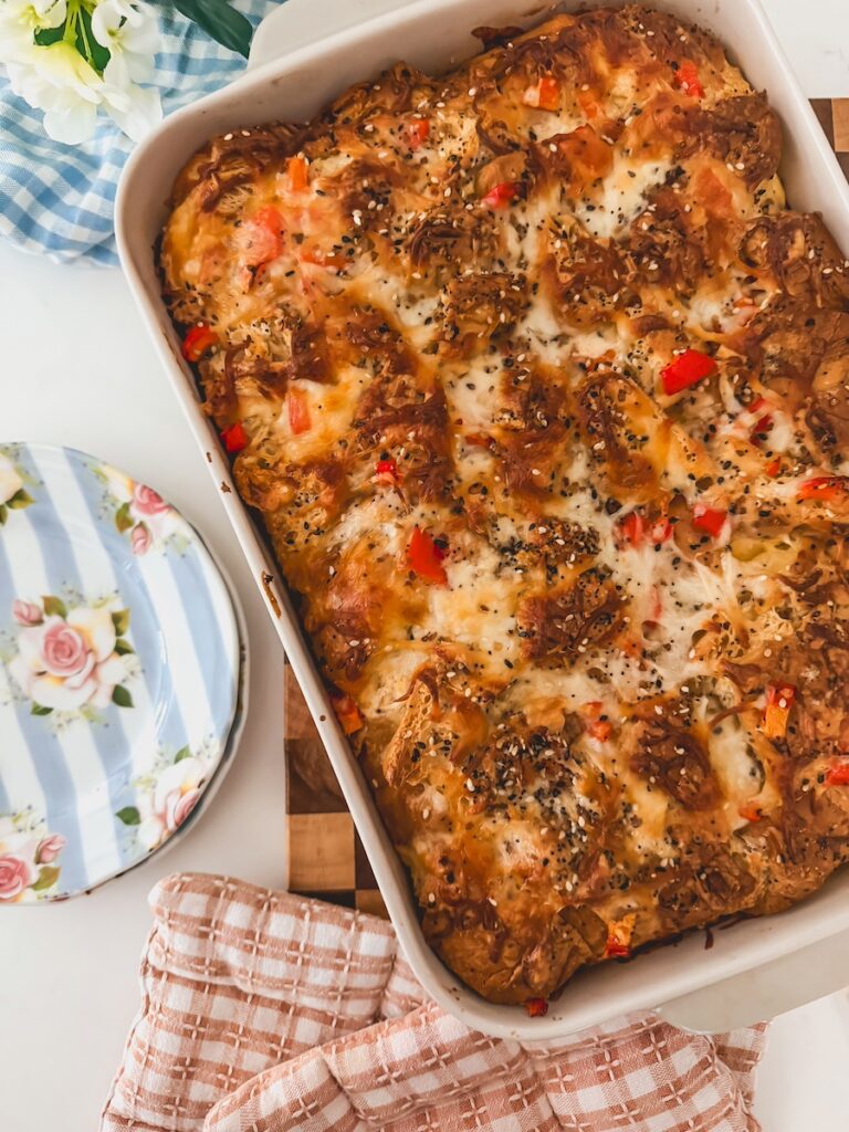 Baked croissant breakfats casserole in a baking dish with blue striped plates on the side.