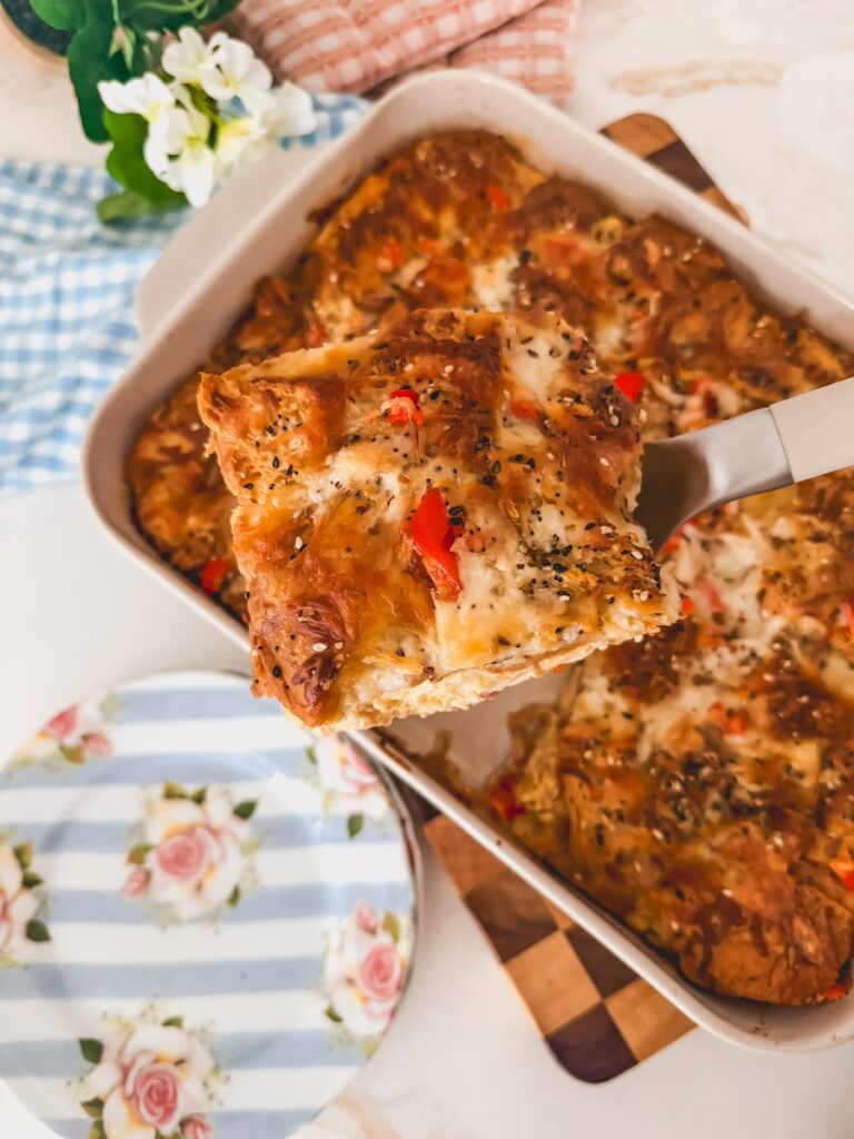 A spatula lifting a piece of croissant breakfast casserole up. Blue striped plates are in the background.