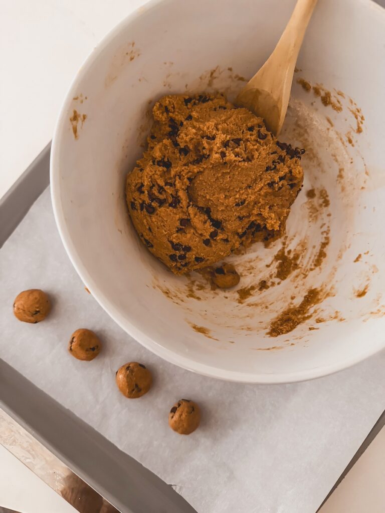 bowl of dough next to baking sheet with cookie dough balls