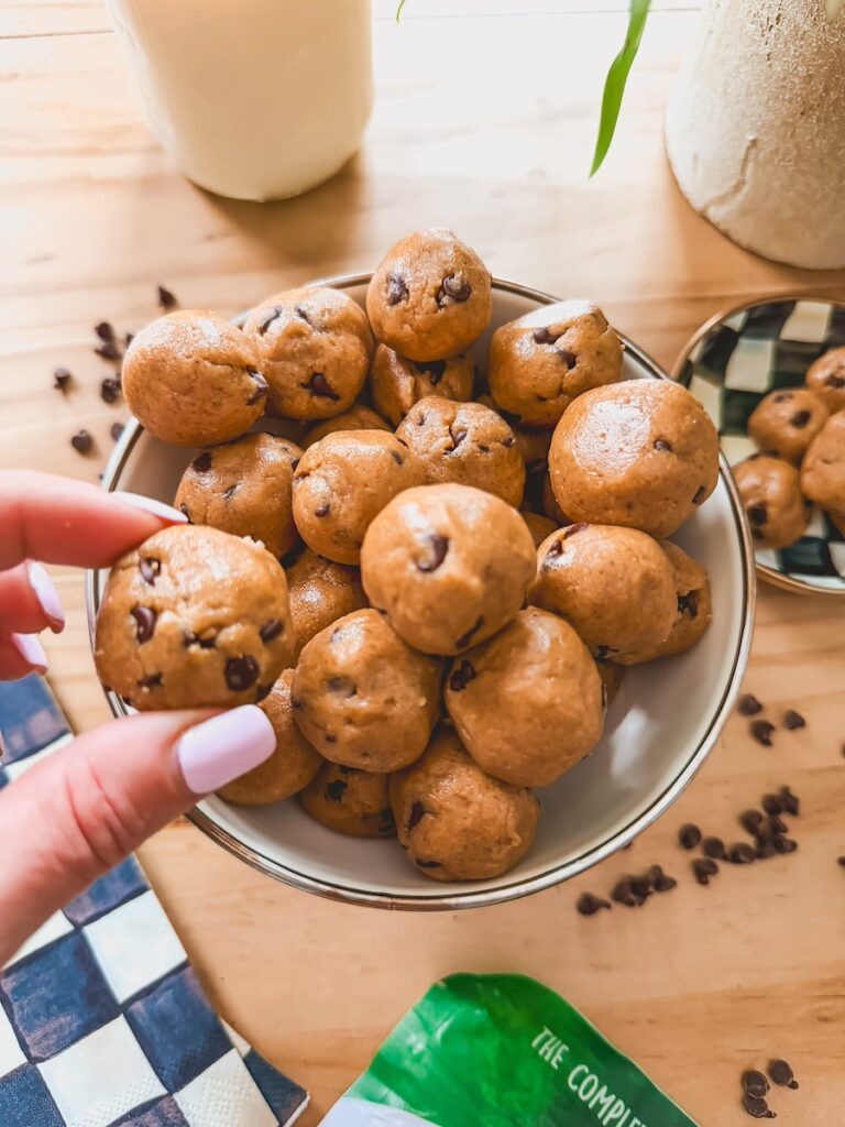 hand holding one cookie dough ball with bowl in the background