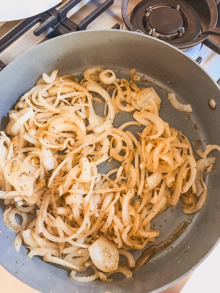 sliced onions starting to cook and caramelize in a pan.