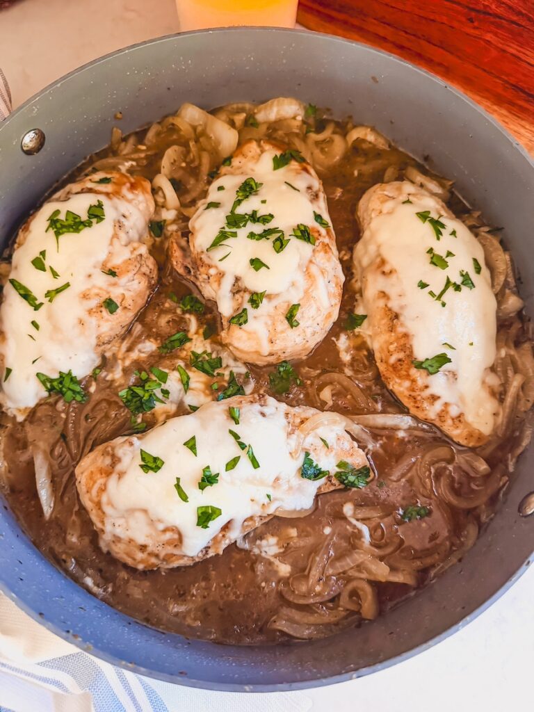 cooked chicken breasts topped with cheese and green herbs in caramelized onion sauce