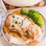 plated serving of french onion chicken with potatoes and broccoli. Pot of french onion chicken on cutting board in background.
