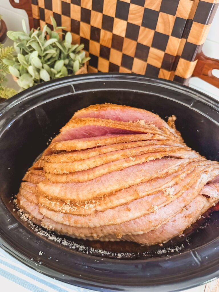 sliced cola ham in slow cooker with checkered cutting board in background