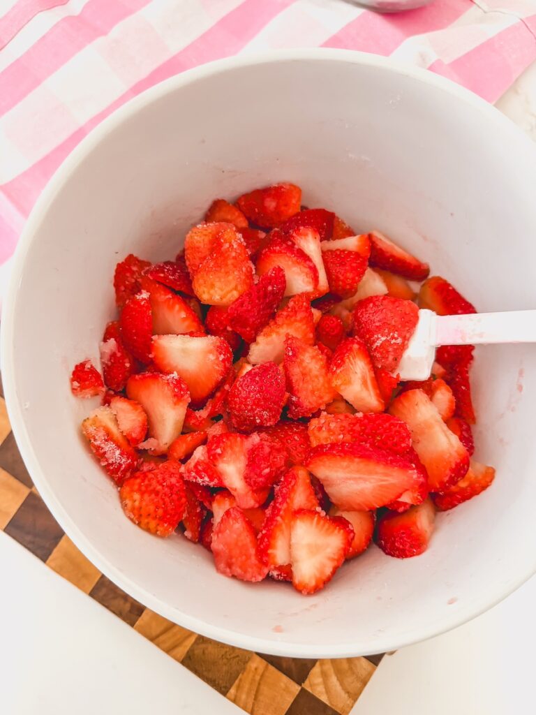 sliced strawberries in white bowl with cutting board and striped pink linen in background