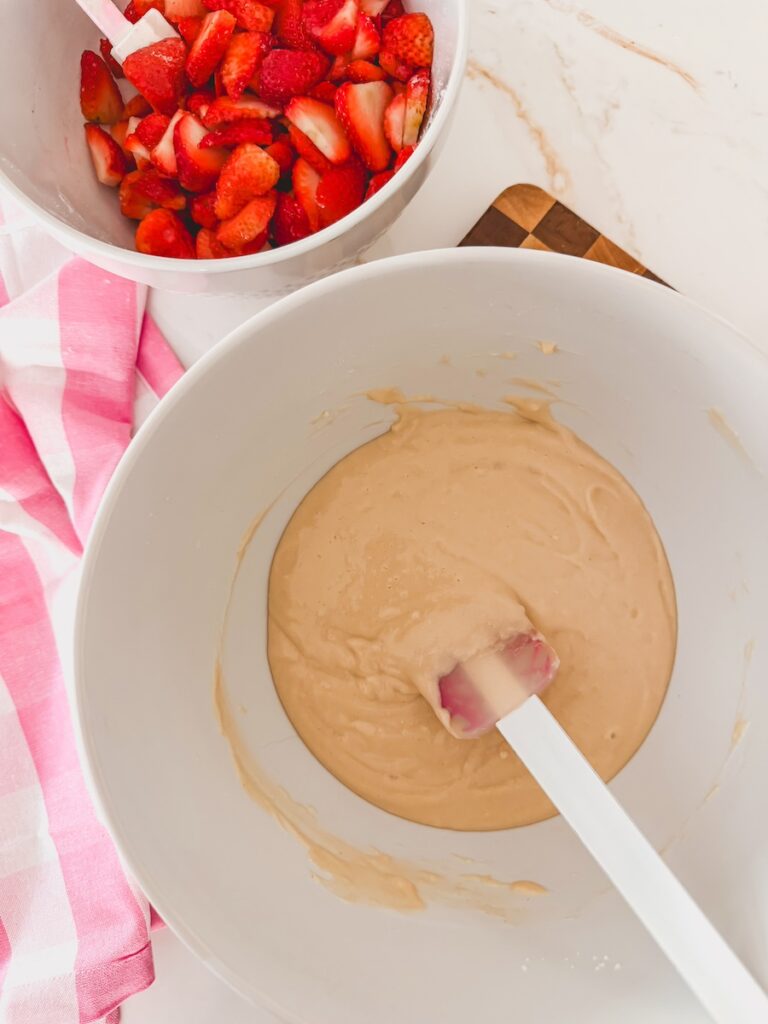 sliced strawberries in white bowl next to cobbler batter in larger white bowl with spatula