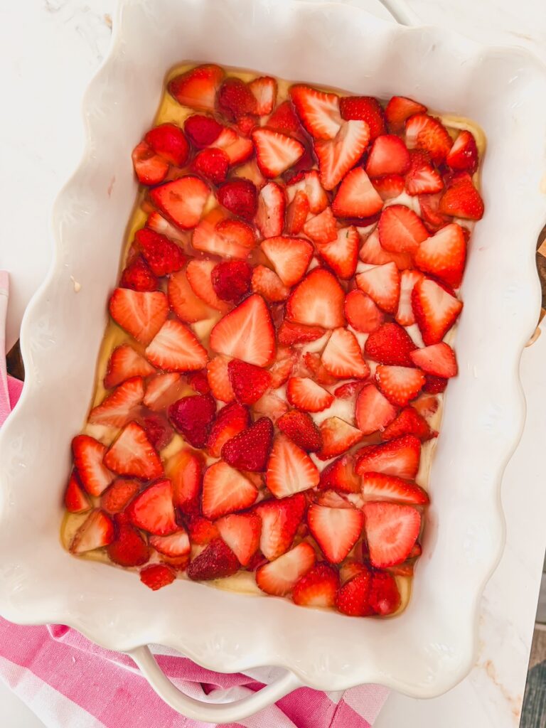 cobbler batter and sliced strawberries in bottom of white baking dish