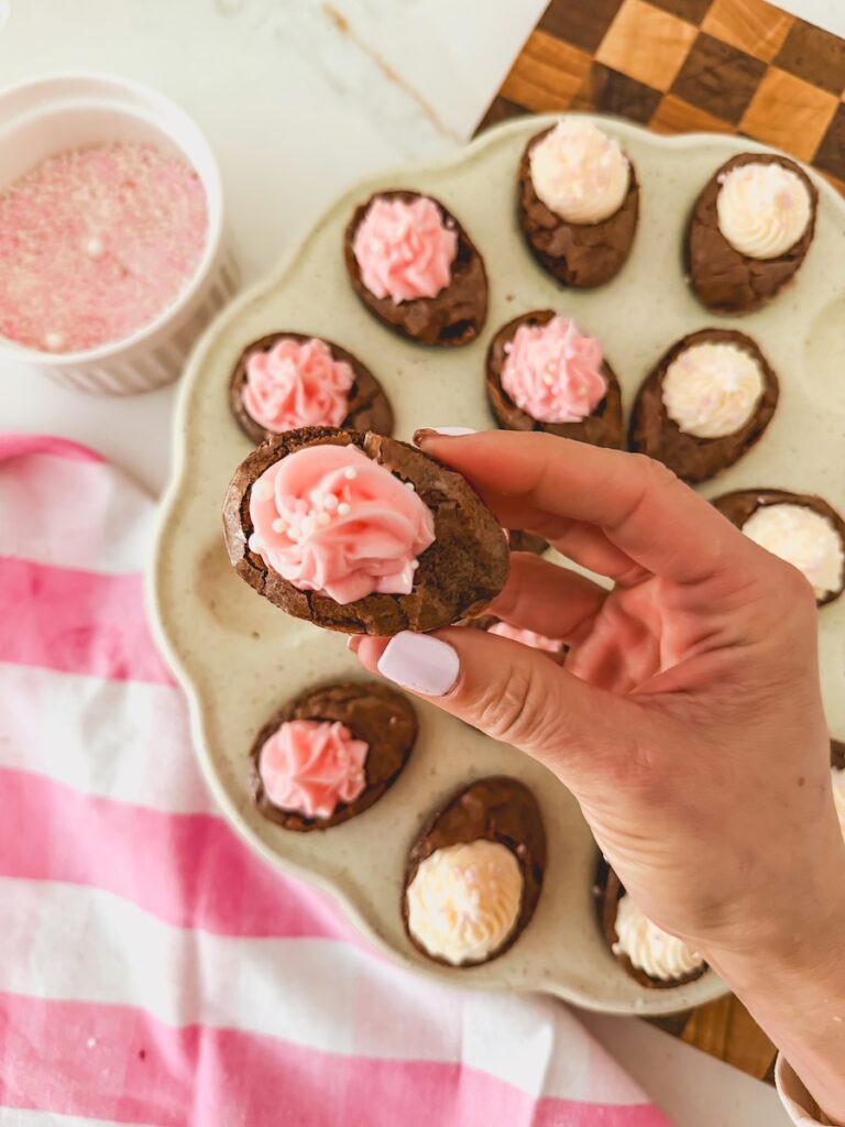 close up of hand holding deviled brownie with pink frosting