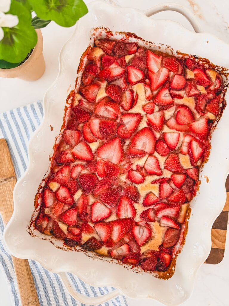 baked strawberry cobbler in white baking dish with green plant in background