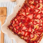 baked strawberry cobbler in white baking dish with wooden spoon on side