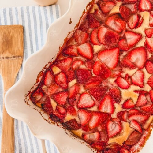 baked strawberry cobbler in white baking dish with wooden spoon on side