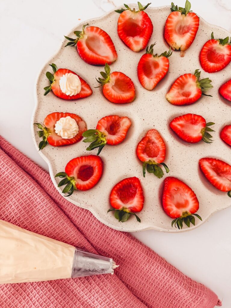 cheesecake filling in a piping bag next to tray of strawberries
