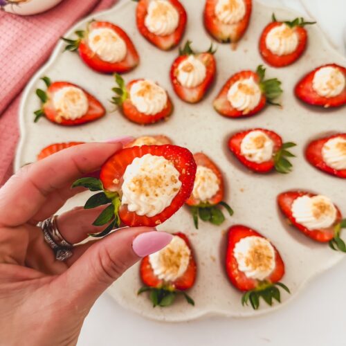 deviled strawberries with cheesecake filling on a tray with a hand holding one